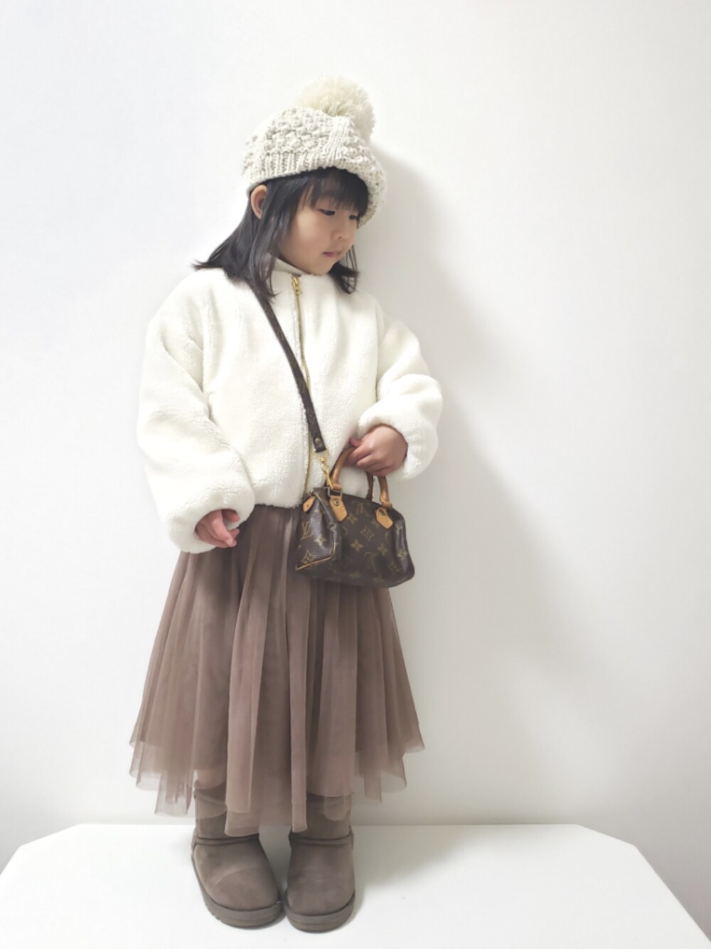 ブラウン系のスカート、グレー系のブーツ、ブラウン系のショルダーバッグを着用したキッズの冬コーディネートの1枚目の写真
