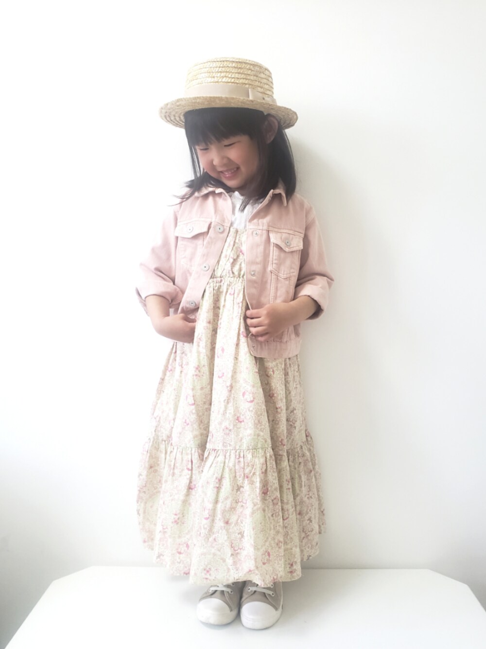 ピンク系のデニムジャケット、ベージュ系のワンピース、ベージュ系のスニーカーを着用したキッズの春コーディネートの1枚目の写真