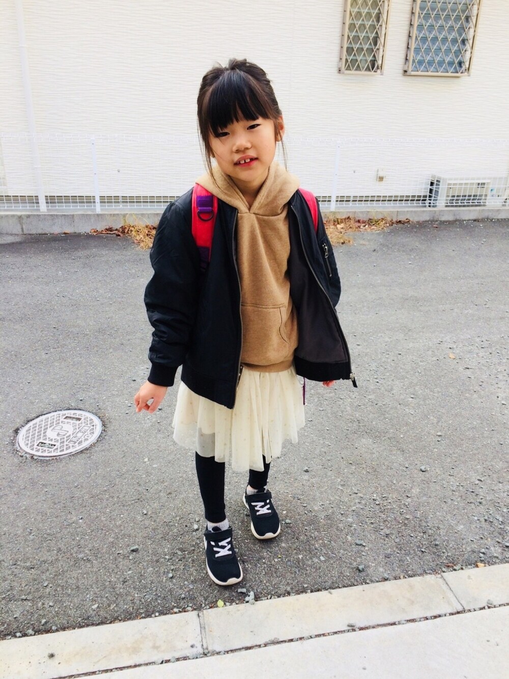 ベージュ系のパーカー、ホワイト系のスカート、ブラック系のスニーカーを着用したキッズの冬コーディネートの1枚目の写真