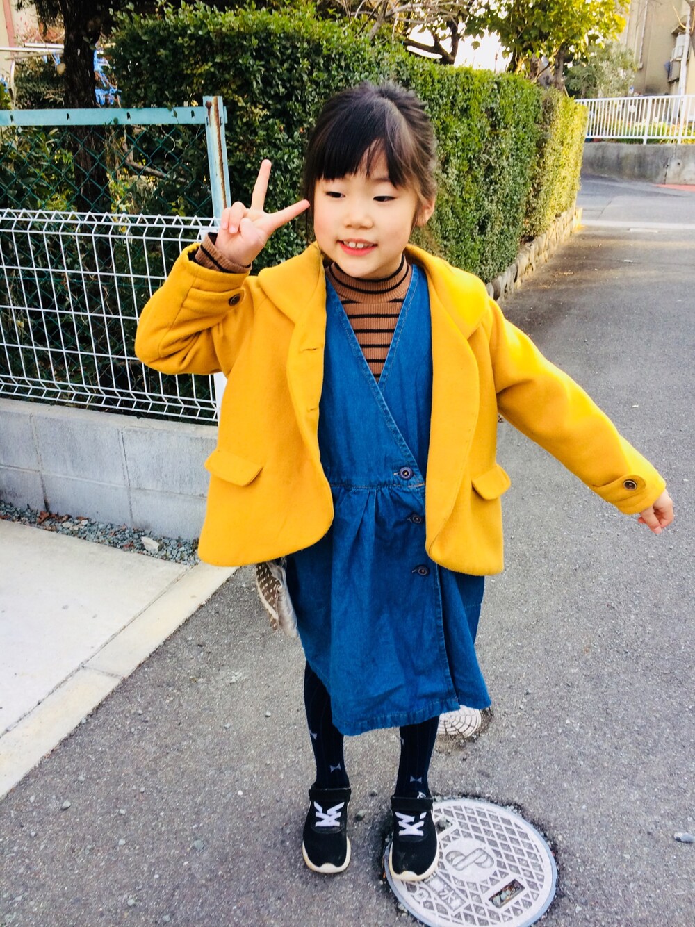 ブラウン系のTシャツ/カットソー、ブルー系のジャンパースカート、ブラック系のスニーカーを着用したキッズの冬コーディネートの1枚目の写真