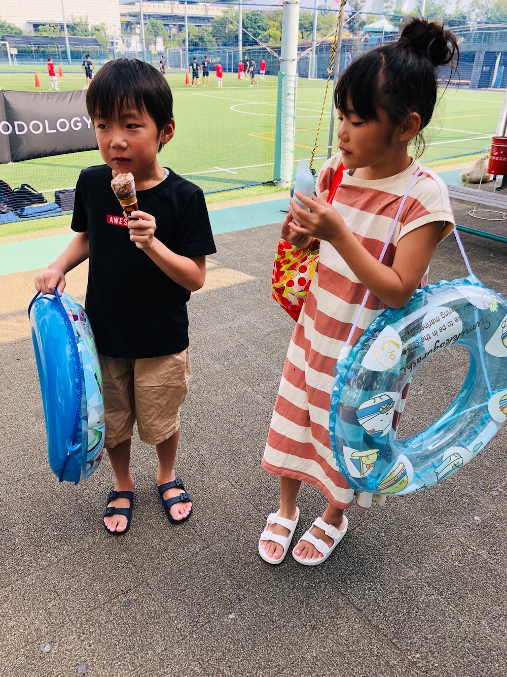 ブルー系のサンダル、ベージュ系のワンピース、ホワイト系のサンダルを着用したキッズの夏コーディネートの1枚目の写真