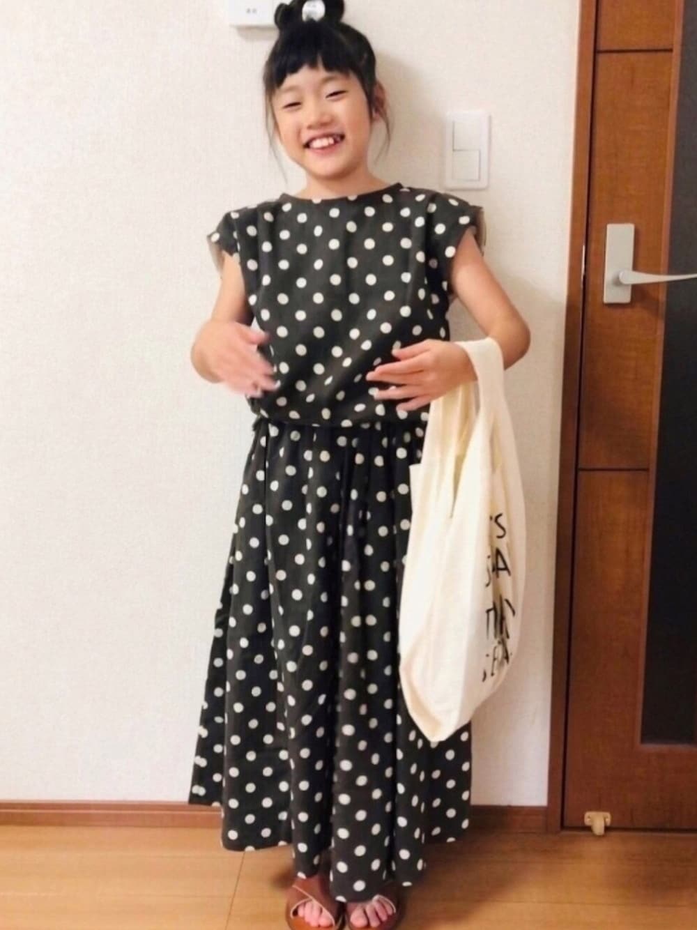 グレー系のスカート、ホワイト系のエコバッグ/サブバッグ、ブラウン系のサンダルを着用したキッズの秋コーディネートの1枚目の写真