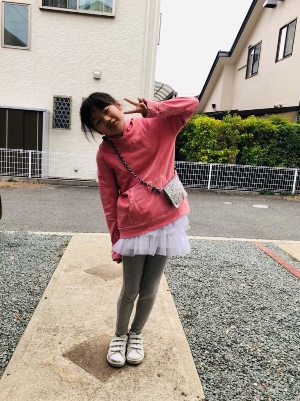 ピンク系のパーカー、ホワイト系のスカート、ホワイト系のスニーカーを着用したキッズの春コーディネートの1枚目の写真