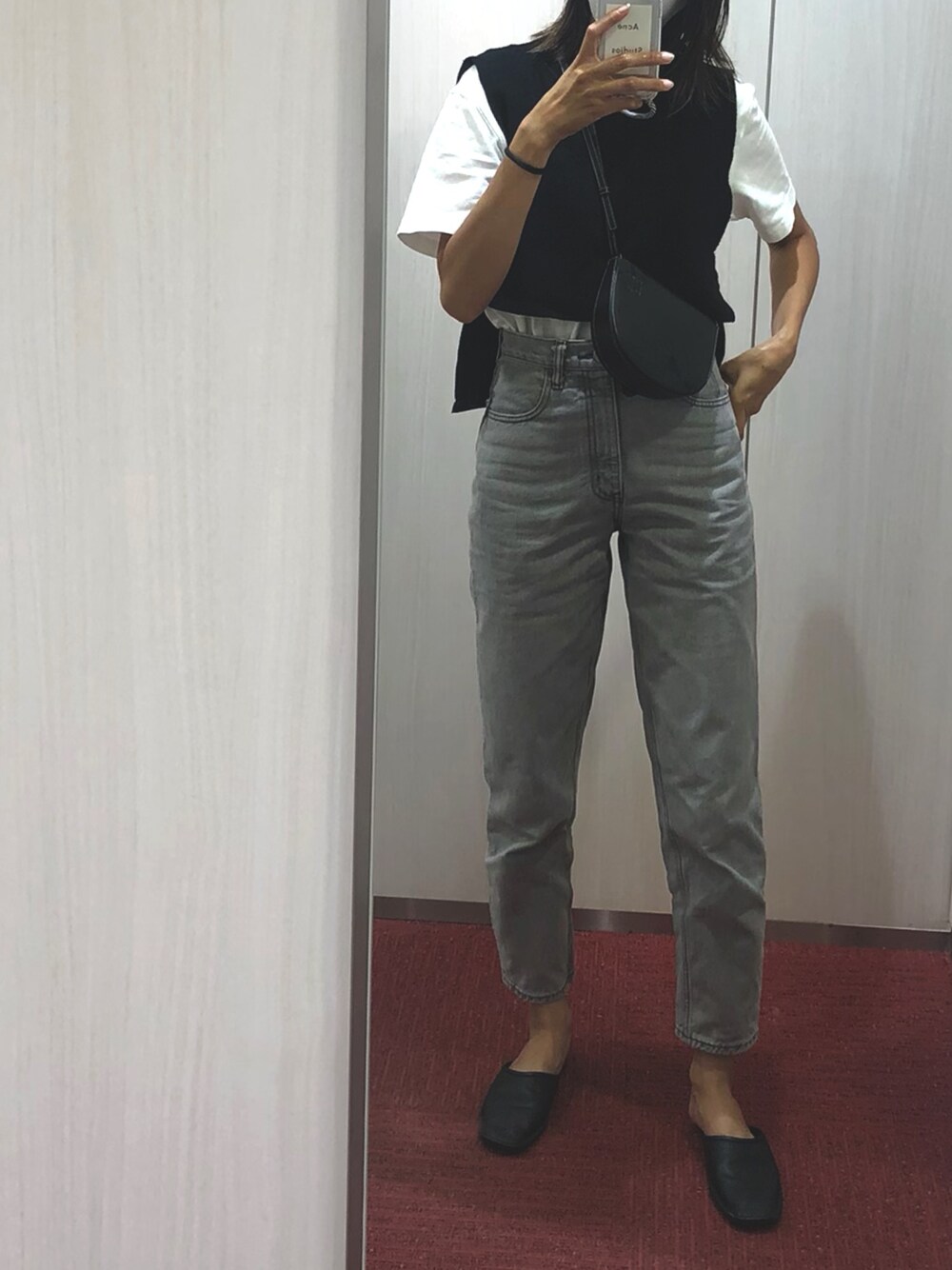 グレー系のデニムパンツ、ブラック系のサンダル、ブラック系のベストを着用したレディースの秋コーディネートの1枚目の写真