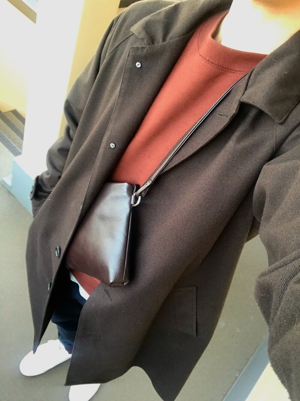 ブラウン系のショルダーバッグ、ホワイト系のスニーカー、ブラウン系のステンカラーコートを着用したメンズの秋コーディネートの1枚目の写真