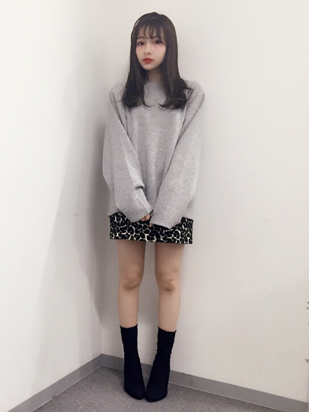 グレー系のニット/セーター、ブラック系のスカート、ブラック系のブーツを着用したレディースの冬コーディネートの1枚目の写真