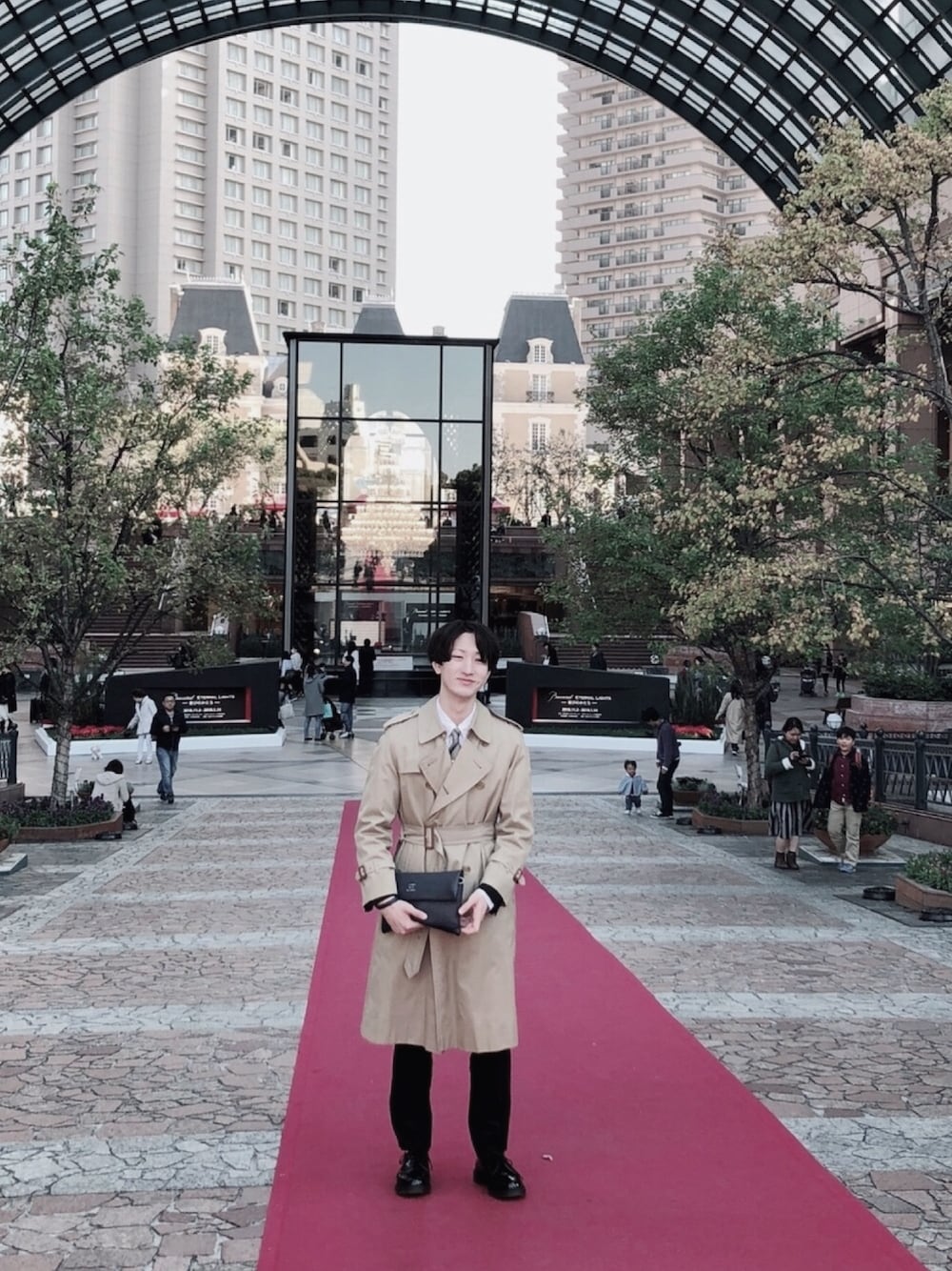 ベージュ系のトレンチコート、ブルー系のクラッチバッグ、ブラック系のドレスシューズを着用したメンズの冬コーディネートの1枚目の写真