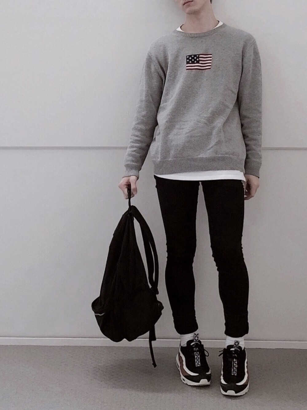 グレー系のニット/セーター、ホワイト系のTシャツ/カットソー、ブラック系のデニムパンツを着用したメンズの秋コーディネートの1枚目の写真