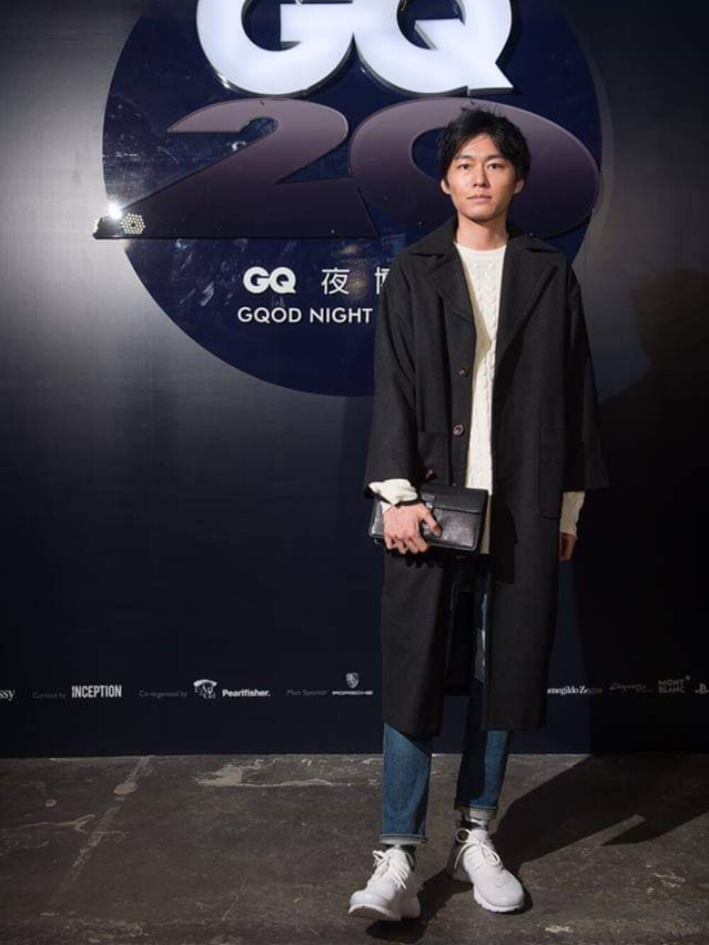 ブラック系のチェスターコート、ブラック系のハンドバッグ、ブルー系のデニムパンツを着用したメンズの秋コーディネートの1枚目の写真