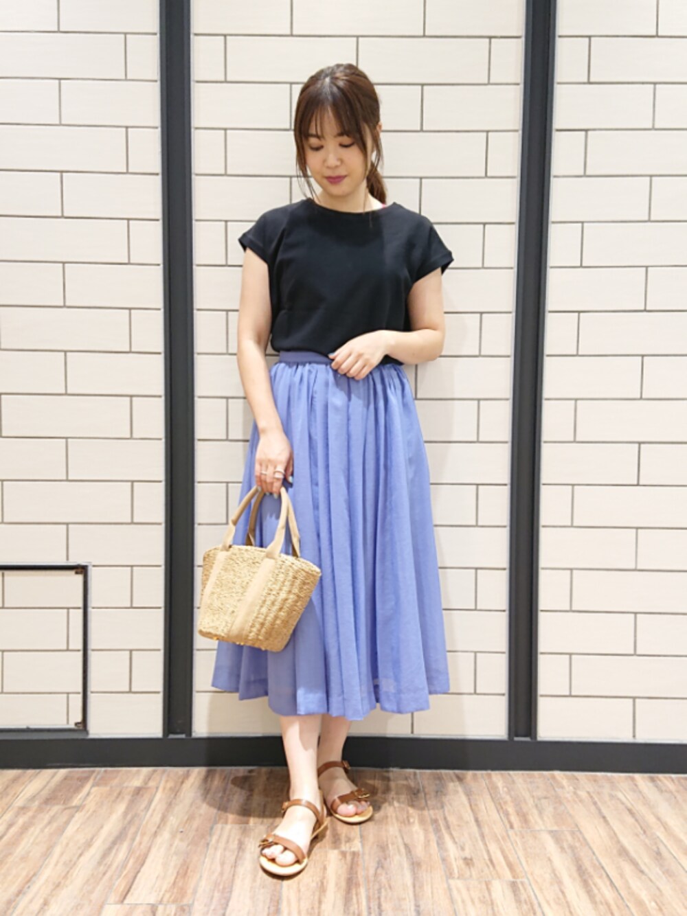 ブラック系のTシャツ/カットソー、ブルー系のスカート、ベージュ系のかごバッグを着用したレディースの夏コーディネートの1枚目の写真