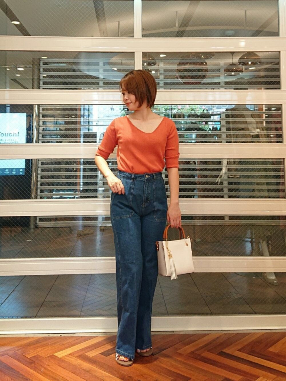 オレンジ系のニット/セーター、ブルー系のパンツ、ホワイト系のトートバッグを着用したレディースの春コーディネートの1枚目の写真