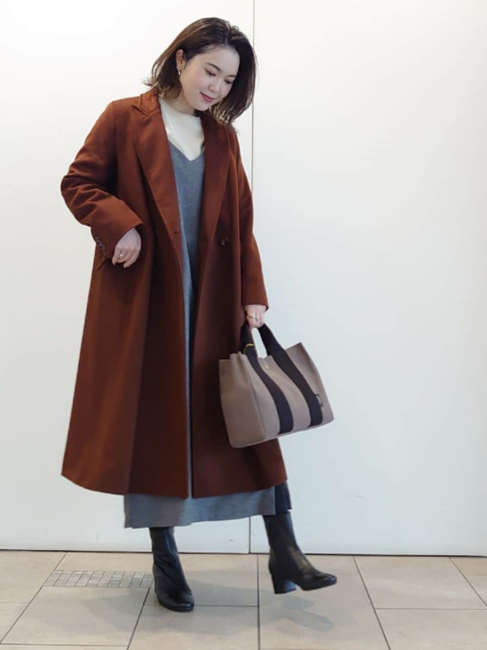 ブラウン系のチェスターコート、グレー系のワンピース、ベージュ系のニット/セーターを着用したレディースの冬コーディネートの1枚目の写真