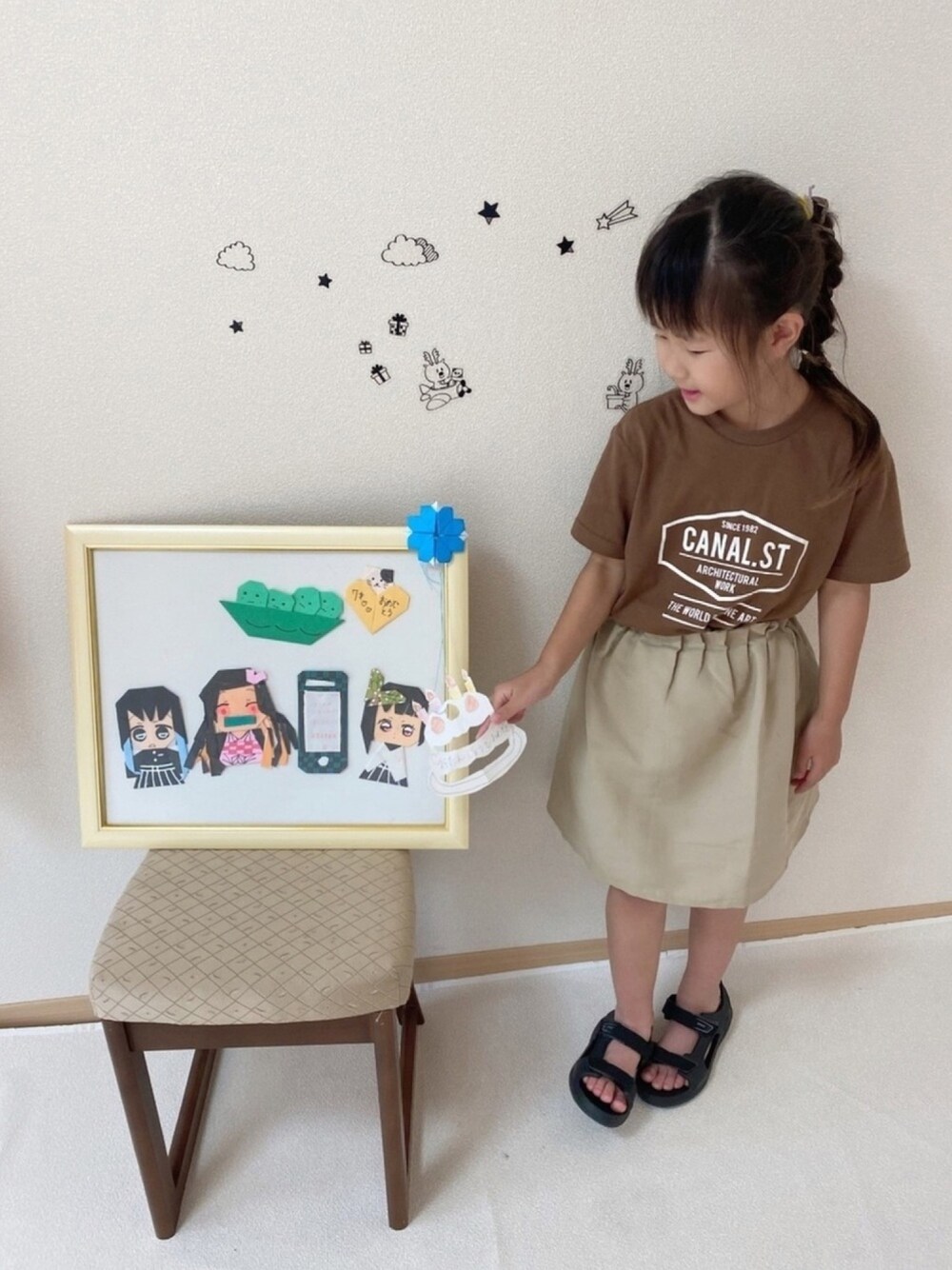 ブラウン系のTシャツ/カットソー、ベージュ系のスカート、ブラック系のサンダルを着用したキッズの夏コーディネートの1枚目の写真