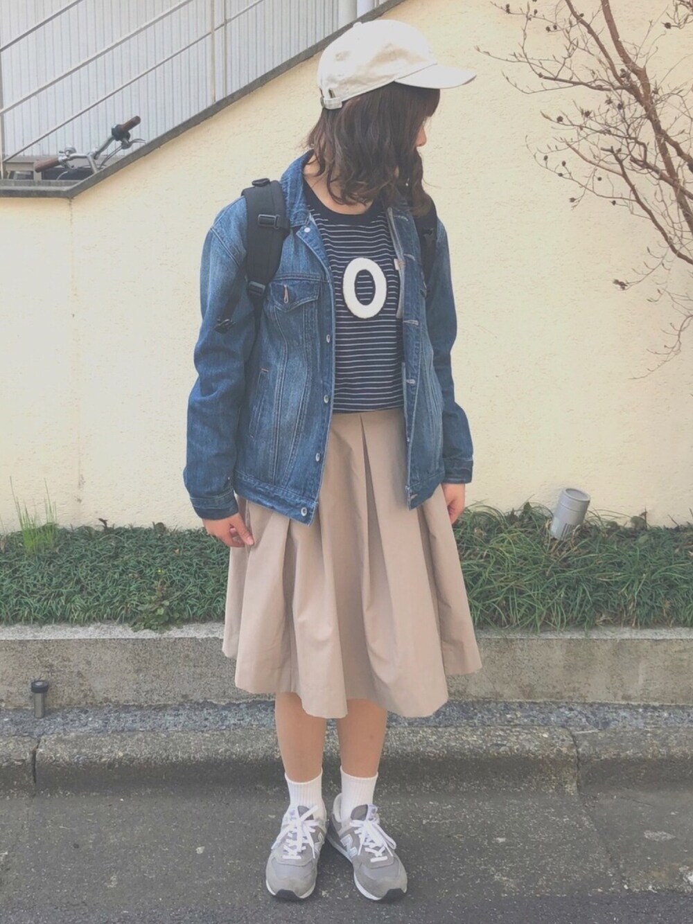 ブルー系のデニムジャケット、ベージュ系のスカート、グレー系のスニーカーを着用したレディースの春コーディネートの1枚目の写真