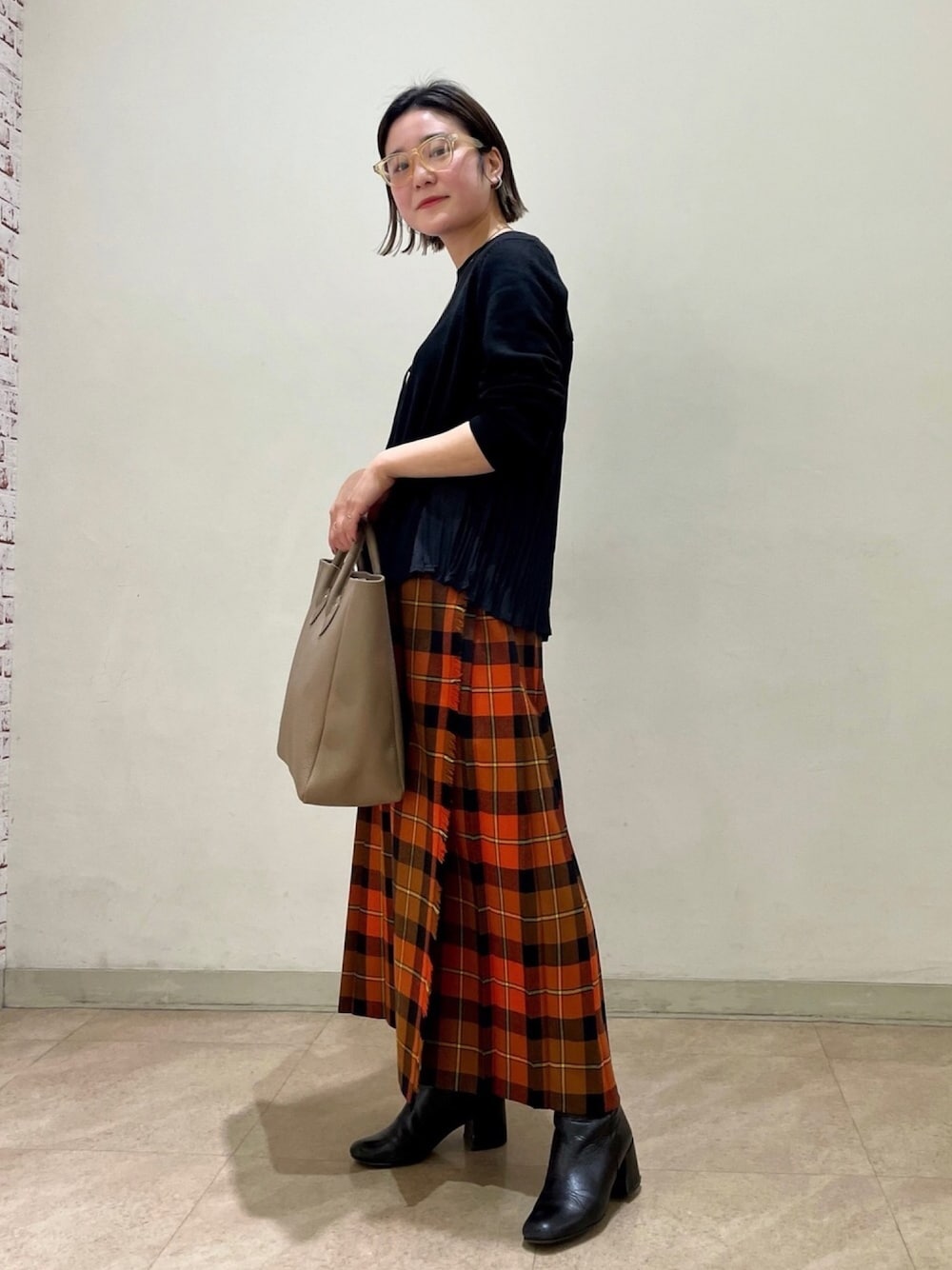 オレンジ系のスカート、ブラック系のニット/セーター、ベージュ系のトートバッグを着用したレディースの冬コーディネートの1枚目の写真