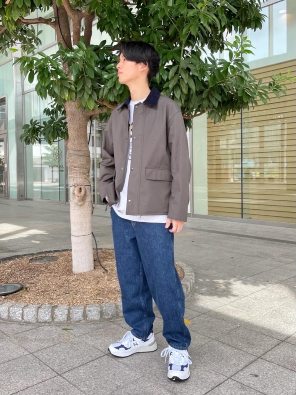 ホワイト系のスニーカー、ブルー系のデニムパンツ、グリーン系のステンカラーコートを着用したメンズの秋コーディネートの1枚目の写真