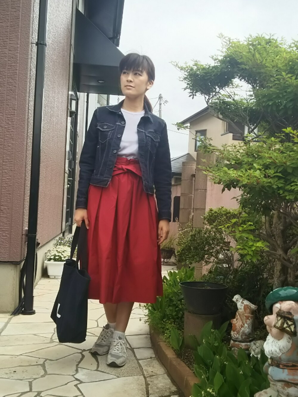 レッド系のスカート、ブルー系のトートバッグ、グレー系のスニーカーを着用したレディースの春コーディネートの1枚目の写真