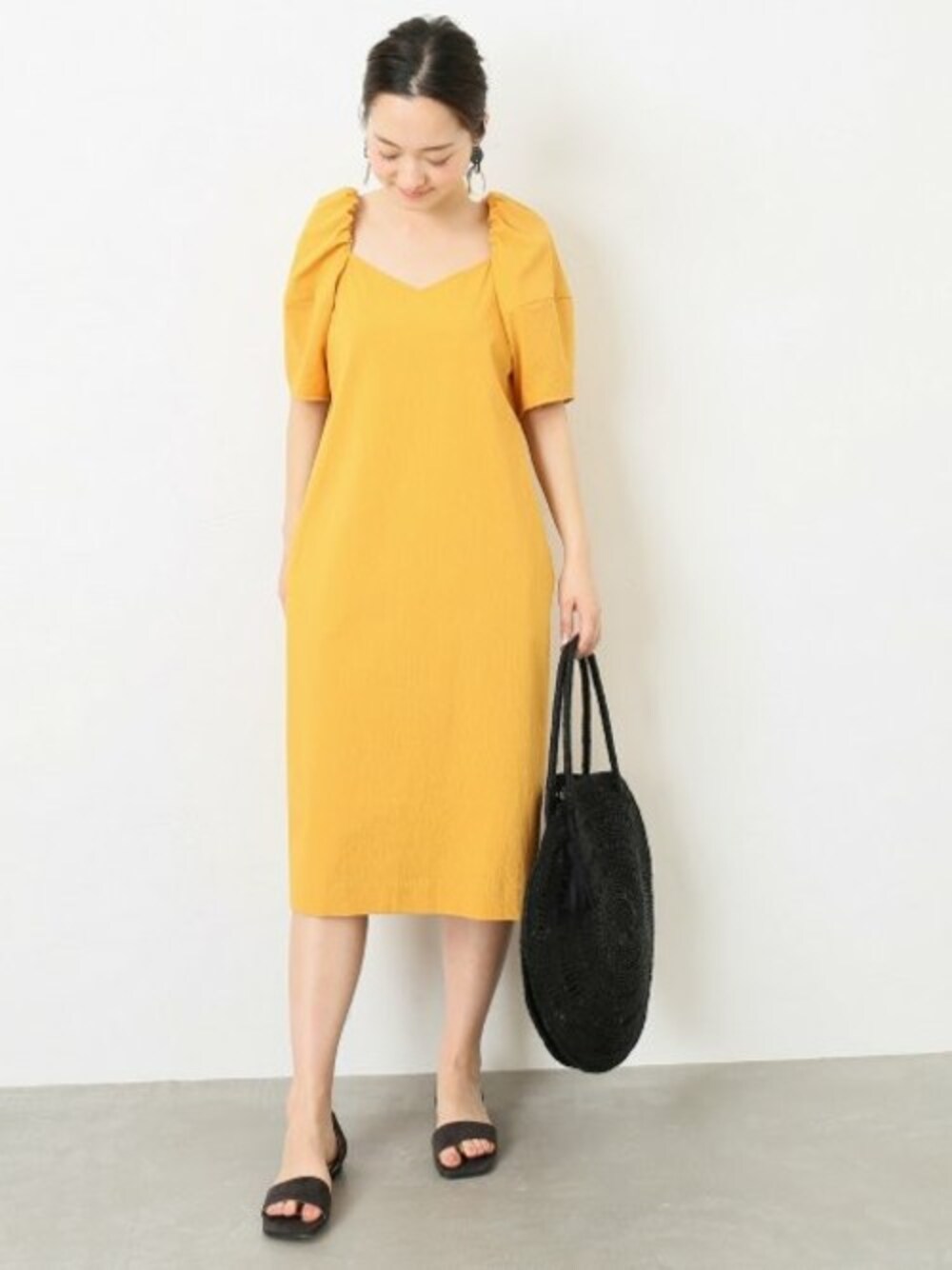 イエロー系のワンピース、グレー系のサンダル、ブラック系のかごバッグを着用したレディースの春コーディネートの1枚目の写真