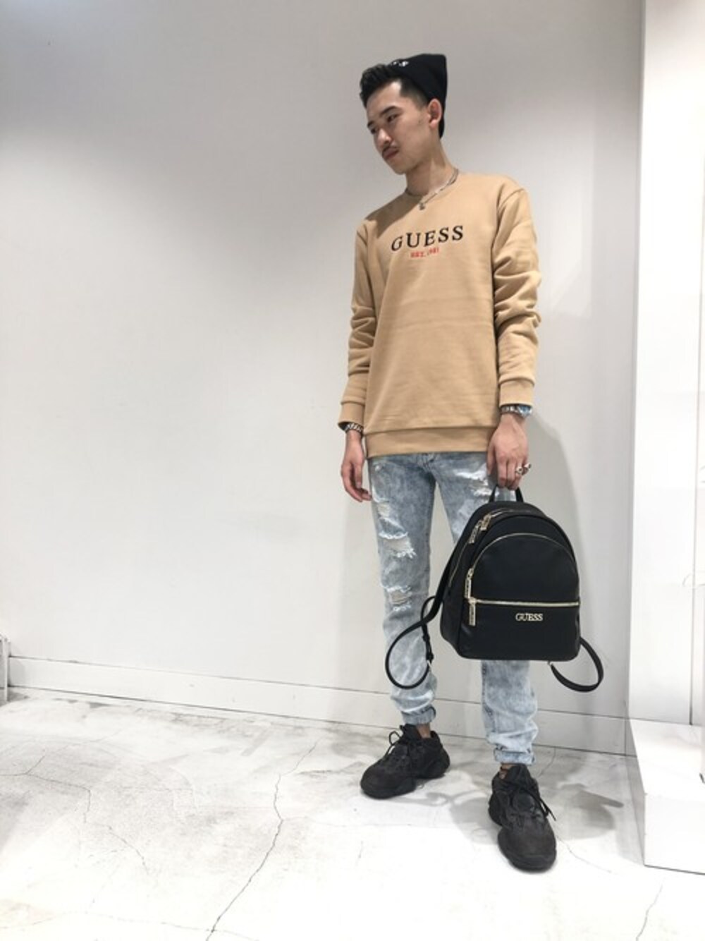 「バックパック、ニット帽、ベージュ、秋のコーデ、ロゴ、ロゴニット、ダメージデニムパンツ、guess」｜「GuessのBLEACH OUT SKINNY DENIM PANT（デニムパンツ、ブルー系）」を使った、GUESS JAPANさん（メンズ・185cm）の秋コーディネートの1枚目の写真