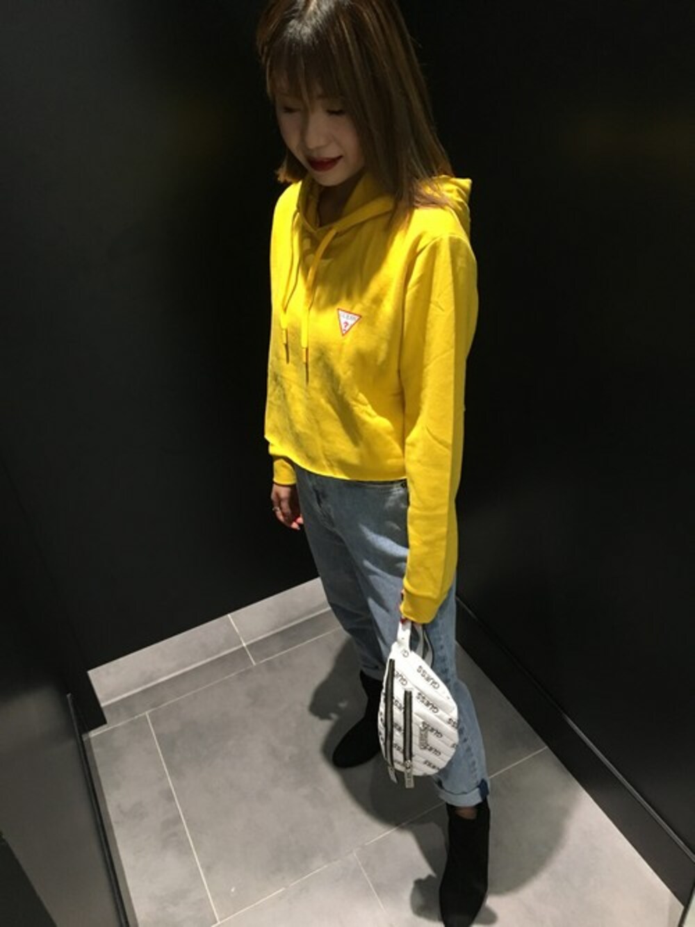 イエロー系のパーカー、ブルー系のデニムパンツ、ホワイト系のボディバッグ/ウエストポーチを着用したレディースの秋コーディネートの1枚目の写真