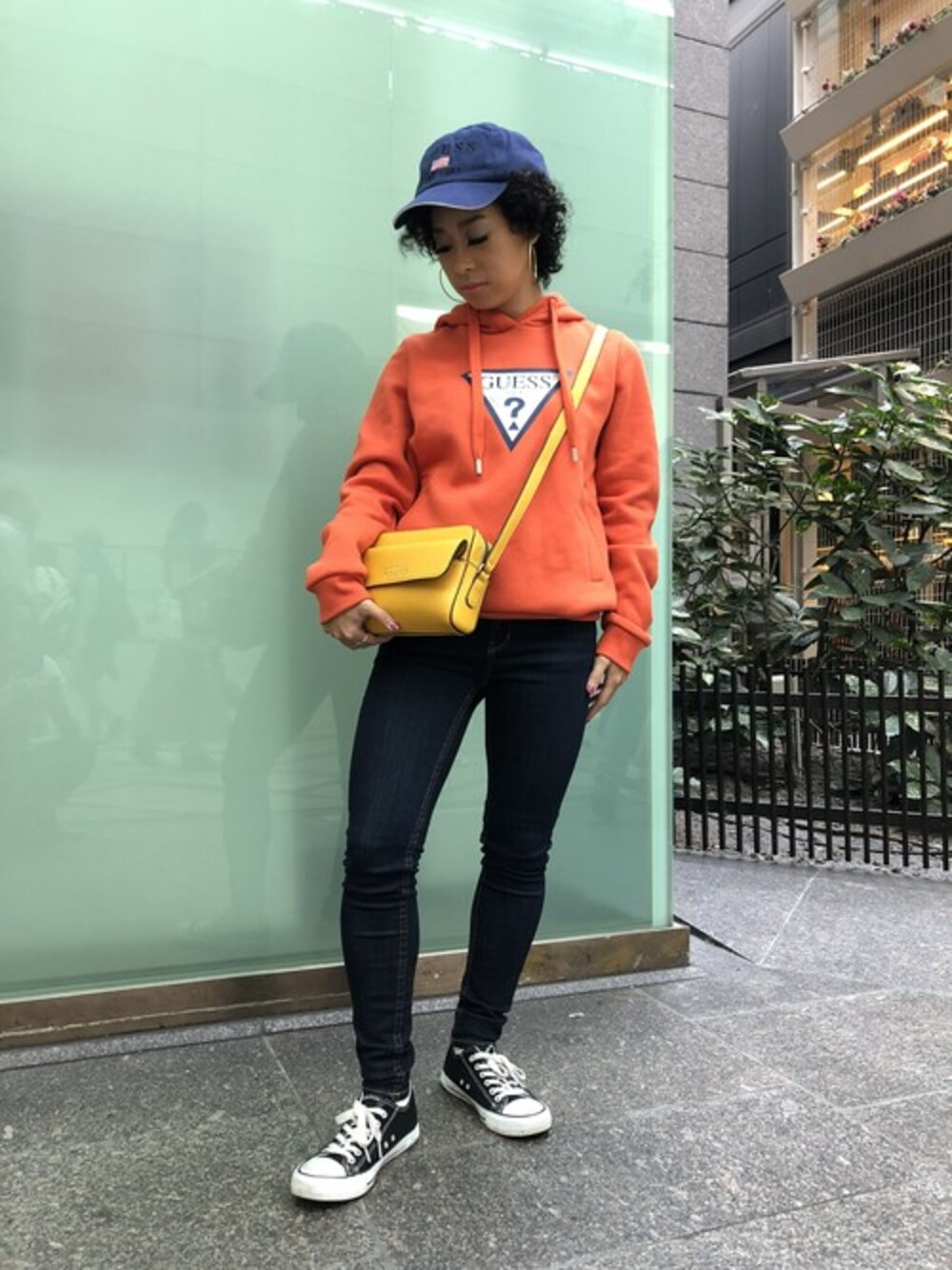 オレンジ系のパーカー、ブルー系のデニムパンツ、イエロー系のショルダーバッグを着用したレディースの秋コーディネートの1枚目の写真