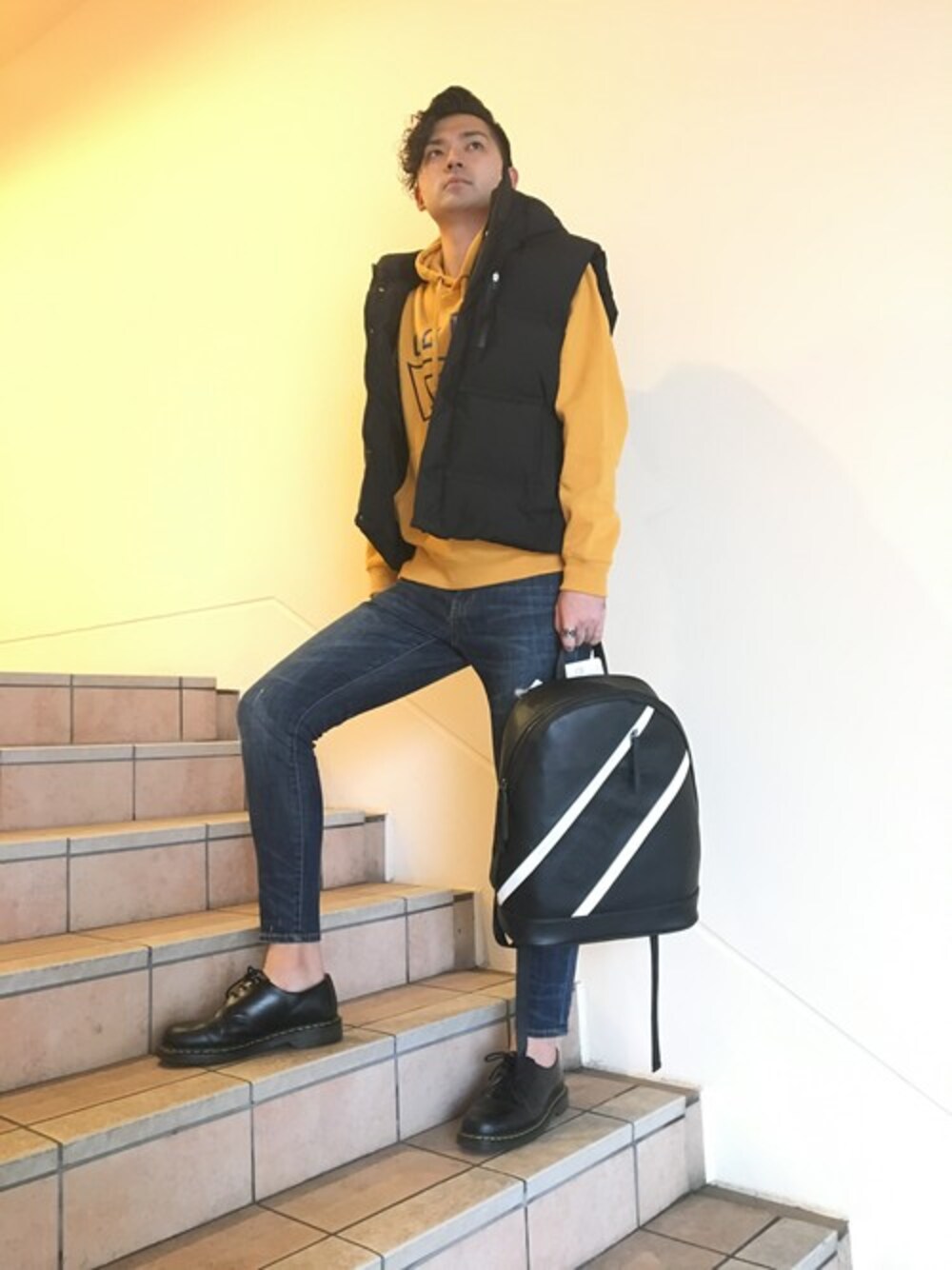 イエロー系のパーカー、ブルー系のデニムパンツ、ブラック系のバックパック/リュックを着用したレディースの秋コーディネートの1枚目の写真