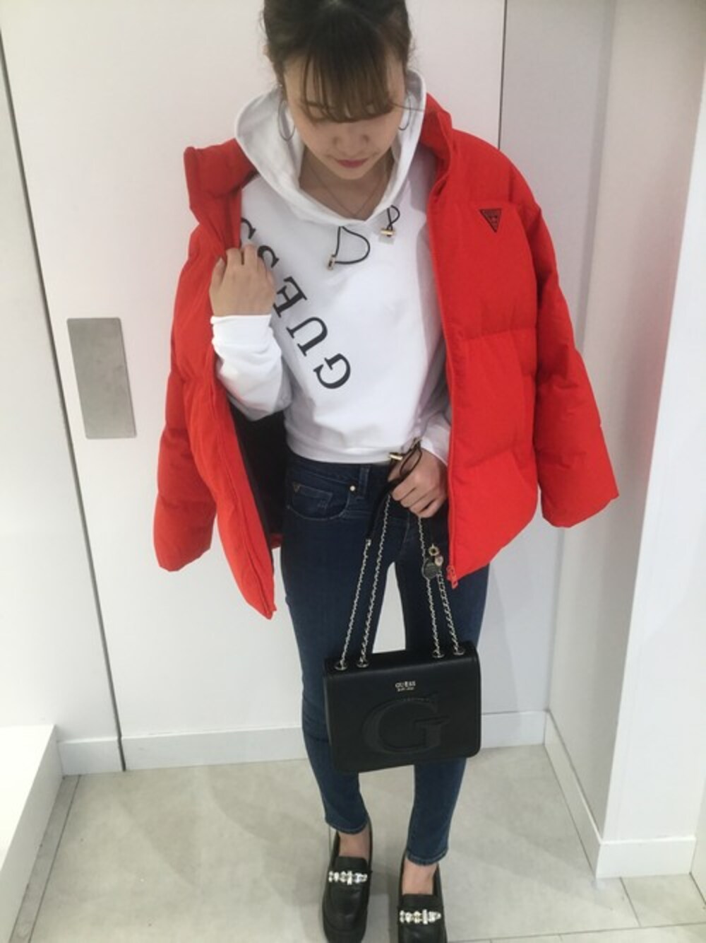 レッド系のダウンジャケット/コート、ブルー系のデニムパンツ、ブラック系のショルダーバッグを着用したレディースの秋コーディネートの1枚目の写真