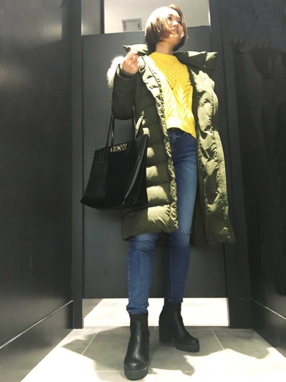 イエロー系のニット/セーター、グリーン系のダウンジャケット/コートを着用したレディースの冬コーディネートの1枚目の写真