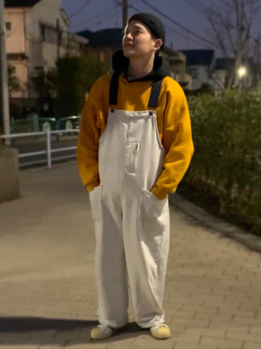 イエロー系のスウェット、ベージュ系のサロペット/オーバーオール、ホワイト系のスニーカーを着用したメンズの冬コーディネートの1枚目の写真