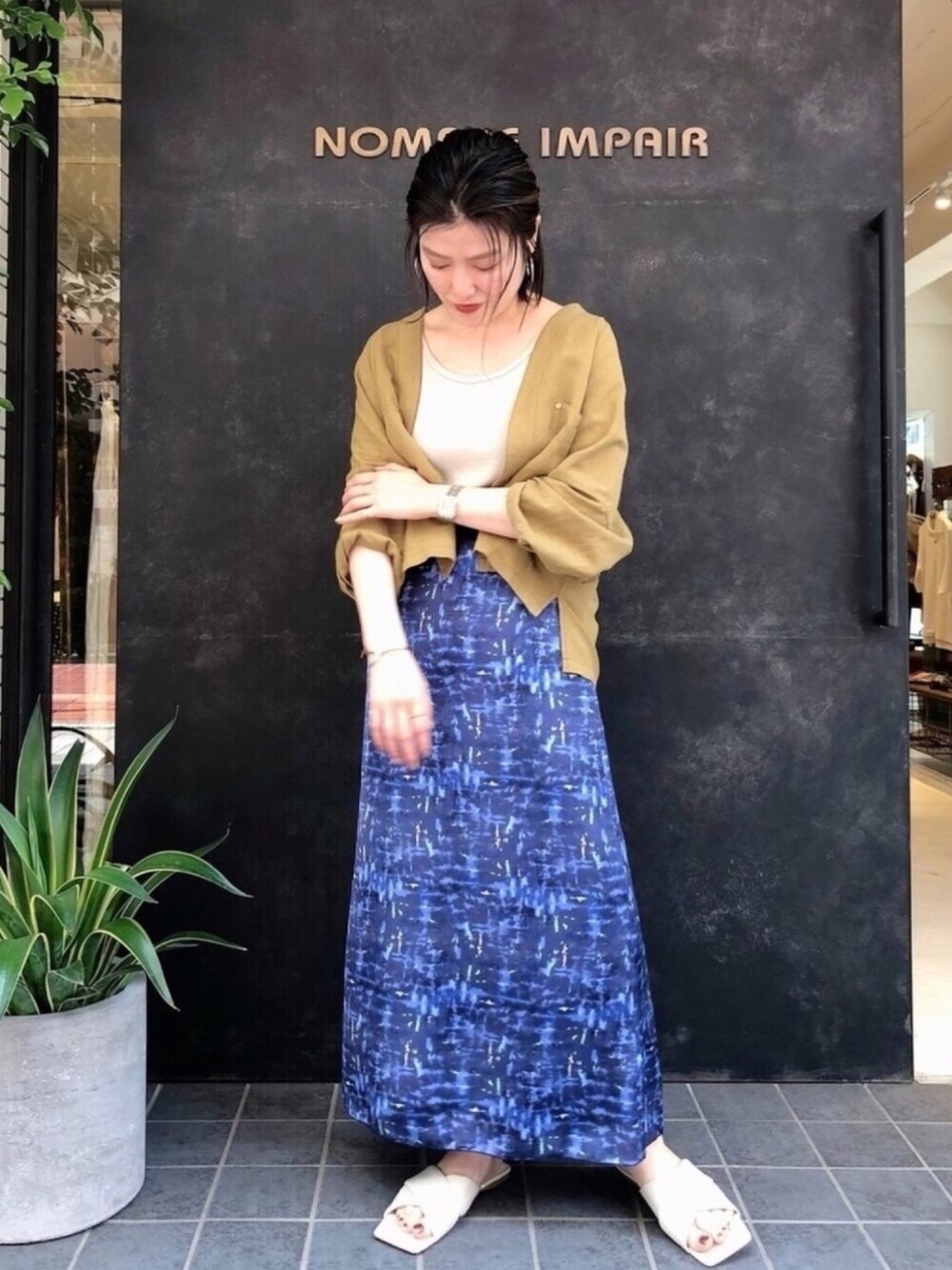 ブルー系のスカート、ベージュ系のタンクトップ、シルバー系のイヤリングを着用したレディースの春コーディネートの1枚目の写真