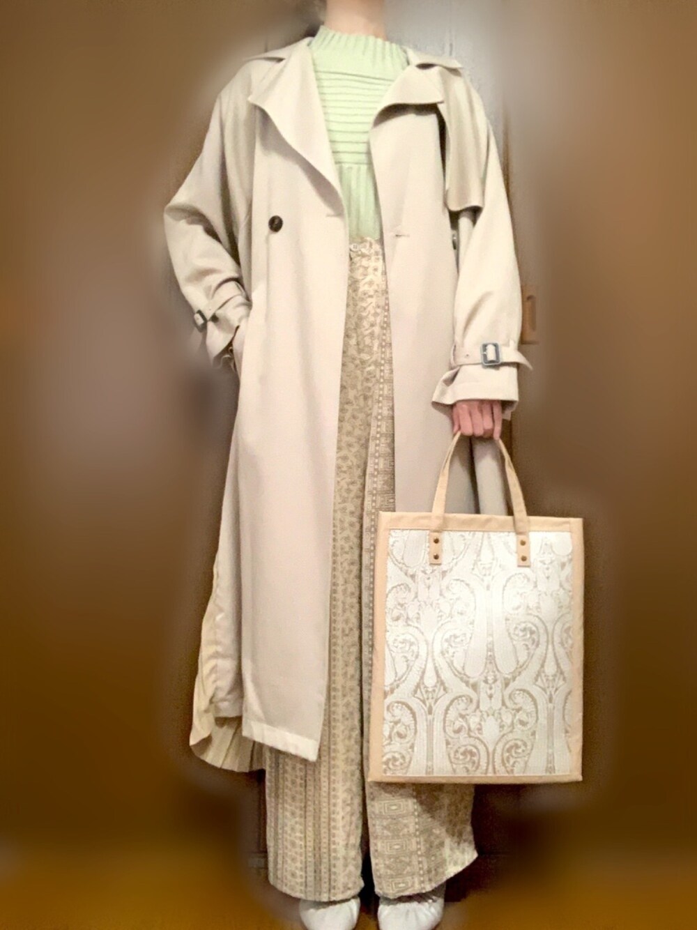 グリーン系のニット/セーター、ベージュ系のトレンチコート、ベージュ系のトートバッグを着用したレディースの春コーディネートの1枚目の写真