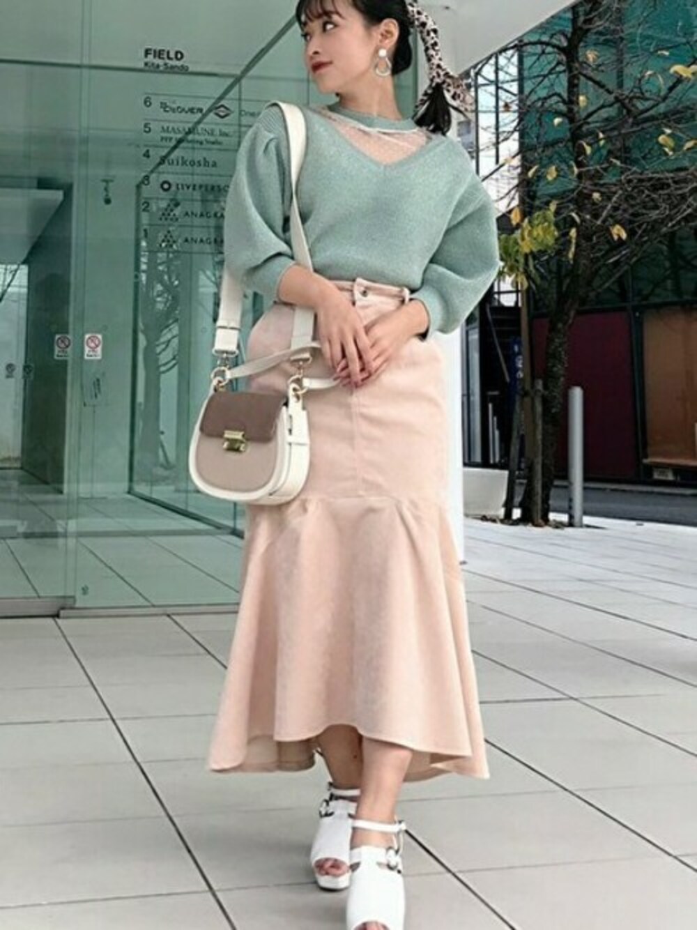 グリーン系のニット/セーター、ベージュ系のスカート、ホワイト系のパンプスを着用したレディースの春コーディネートの1枚目の写真