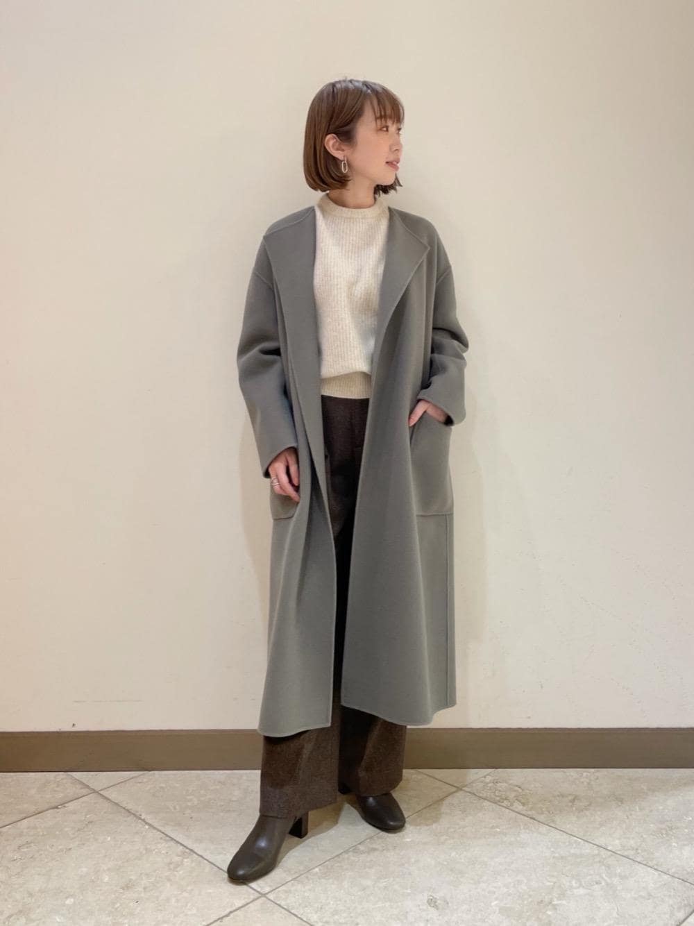 グレー系のノーカラーコート、ブラウン系のブーツ、ブラウン系のその他パンツを着用したレディースの冬コーディネートの1枚目の写真