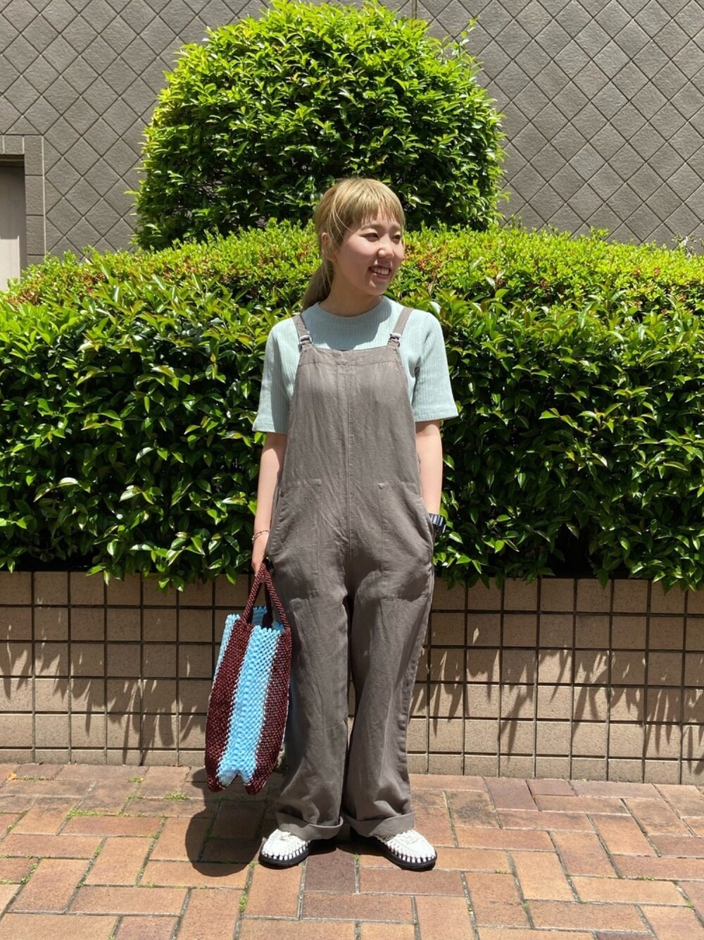 グレー系のサロペット/オーバーオール、グリーン系のTシャツ/カットソー、ホワイト系のサンダルを着用したレディースの春コーディネートの1枚目の写真
