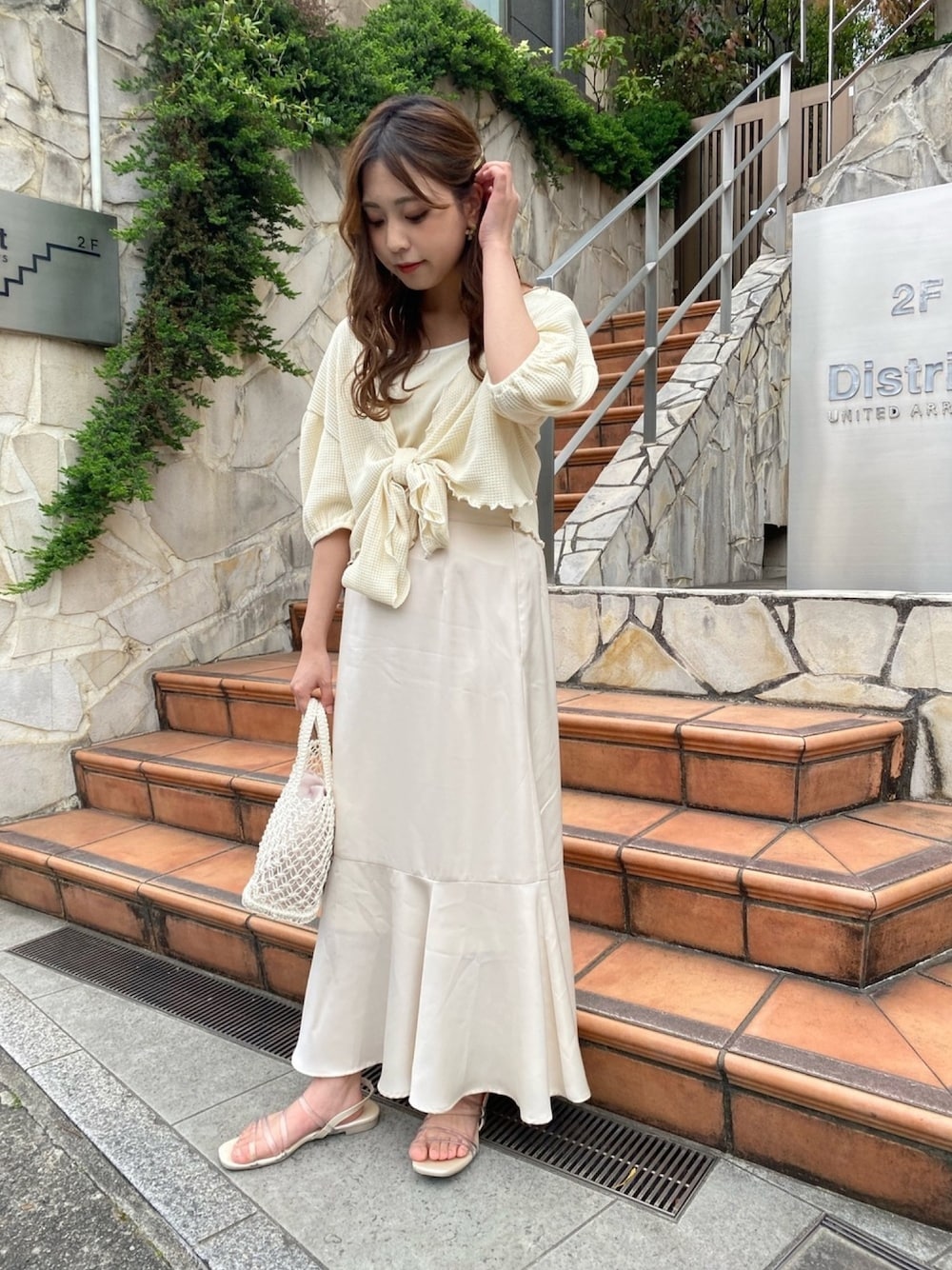 イエロー系のアンサンブル、ホワイト系のスカートを着用したレディースの春コーディネートの1枚目の写真