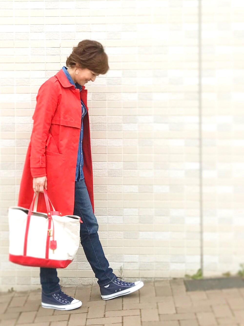 レッド系のトレンチコート、ブルー系のスニーカー、ブルー系のデニムパンツを着用したレディースの春コーディネートの1枚目の写真