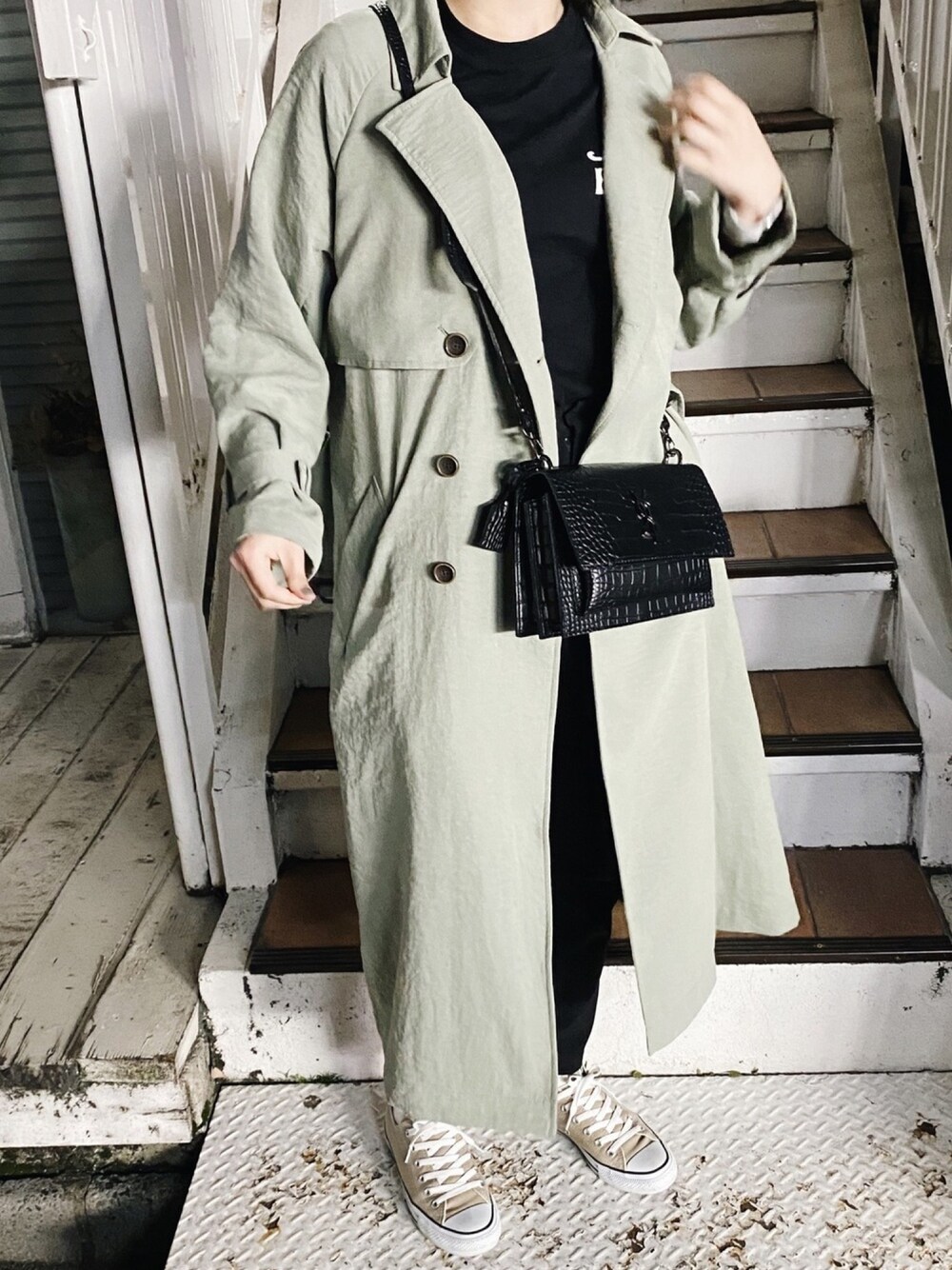 グリーン系のトレンチコート、ベージュ系のスニーカー、ブラック系のパンツを着用したレディースの春コーディネートの1枚目の写真