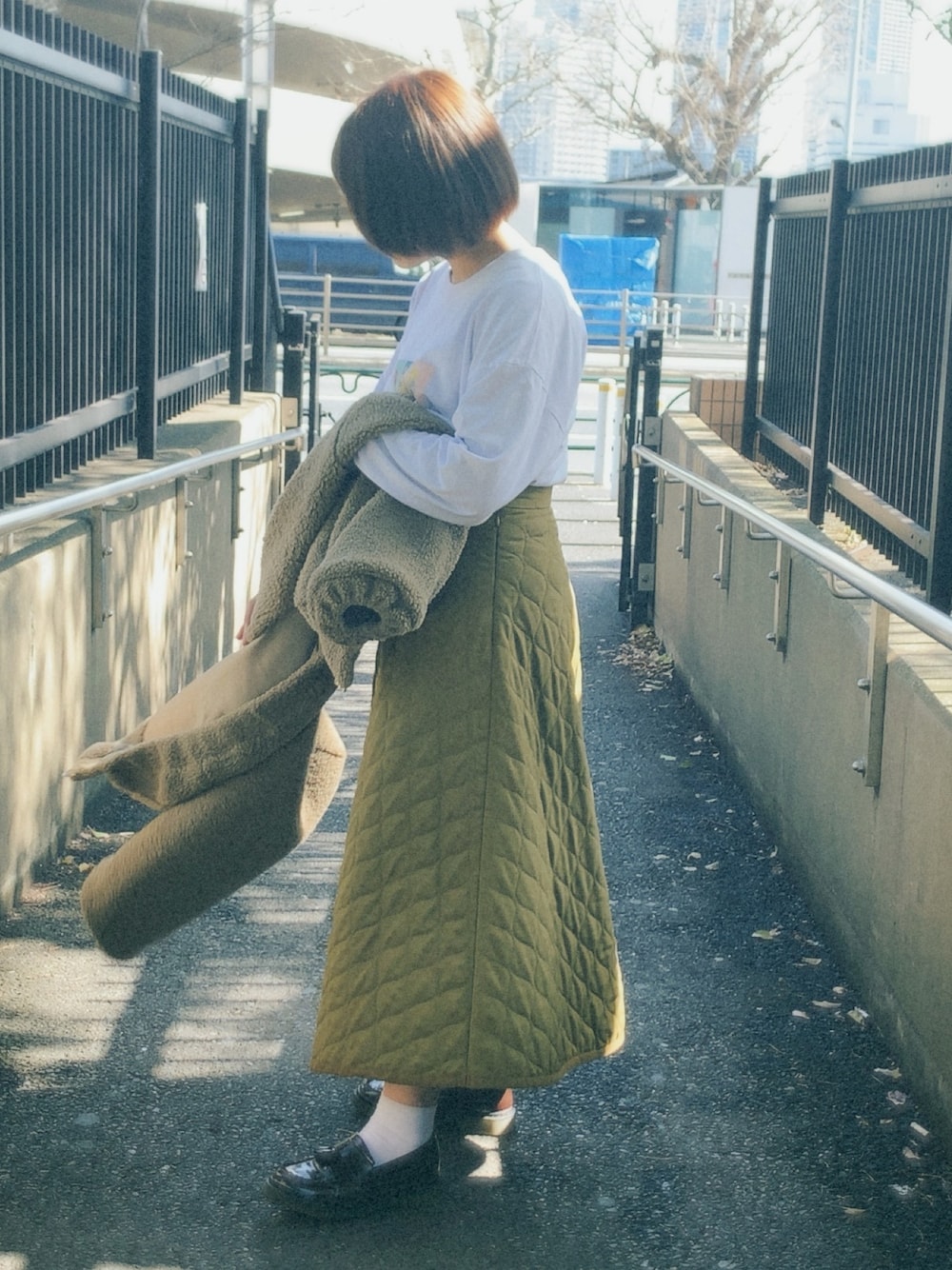 イエロー系のスカート、ホワイト系のTシャツ/カットソー、ブラウン系のローファーを着用したレディースの春コーディネートの1枚目の写真