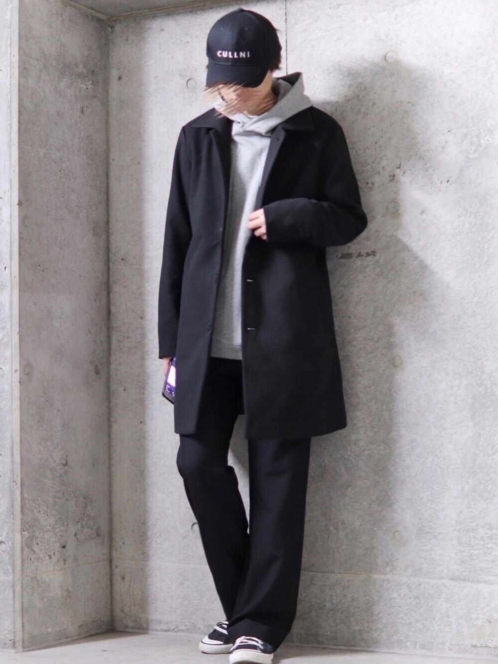 ブラック系のステンカラーコート、ブラック系のスラックス、ブラック系のスニーカーを着用したメンズの秋コーディネートの1枚目の写真