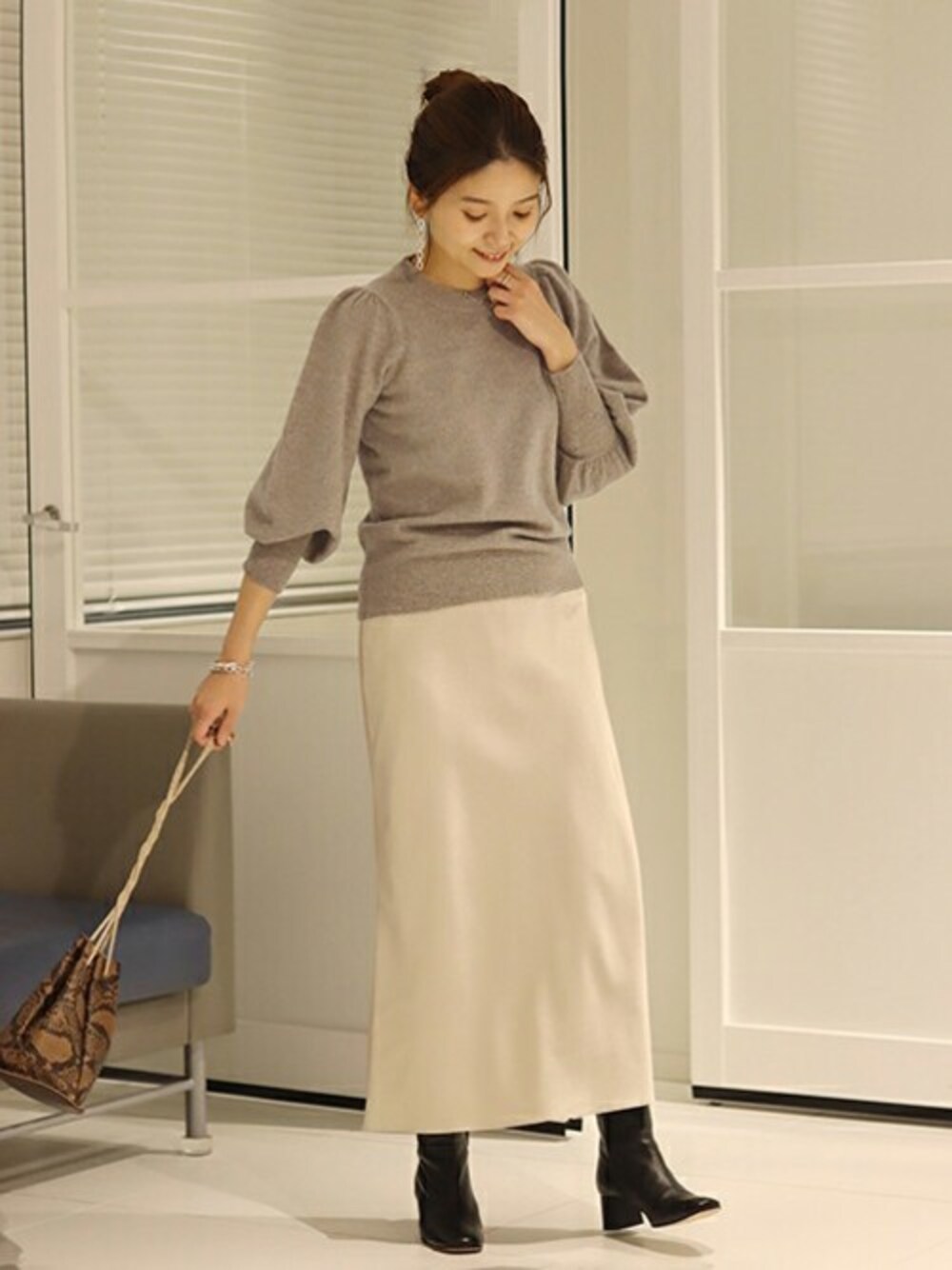 ブラウン系のニット/セーター、ベージュ系のスカート、ブラウン系のショルダーバッグを着用したレディースの秋コーディネートの1枚目の写真