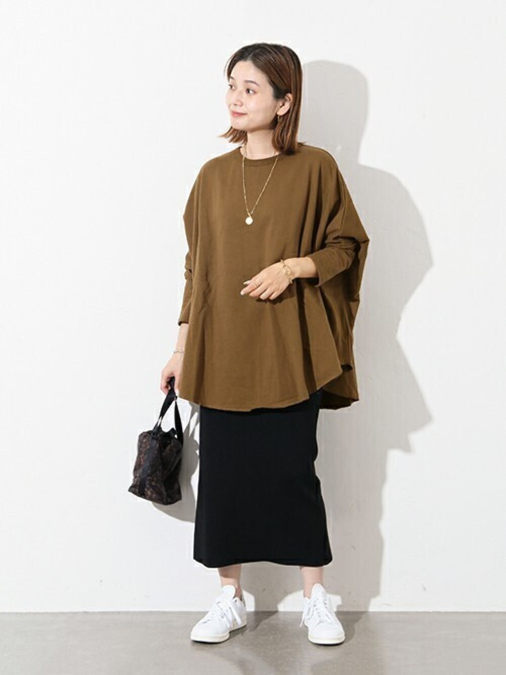 グリーン系のTシャツ/カットソー、ブラック系のスカート、グレー系のスニーカーを着用したレディースの秋コーディネートの1枚目の写真