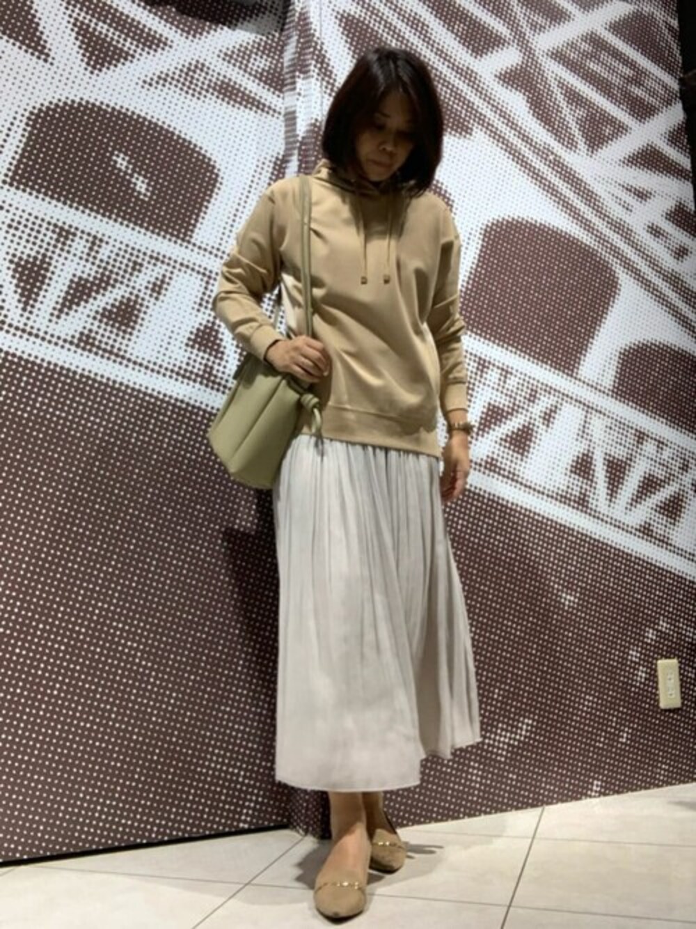イエロー系のパーカー、ベージュ系のスカート、ベージュ系のトートバッグを着用したレディースの秋コーディネートの1枚目の写真