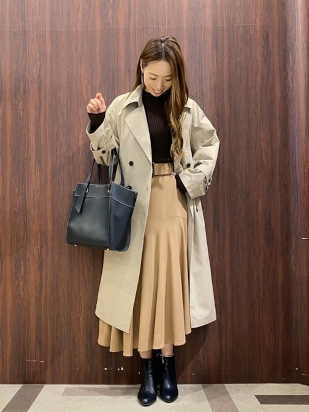 ベージュ系のトレンチコート、イエロー系のスカート、ブラック系のニット/セーターを着用したレディースの秋コーディネートの1枚目の写真