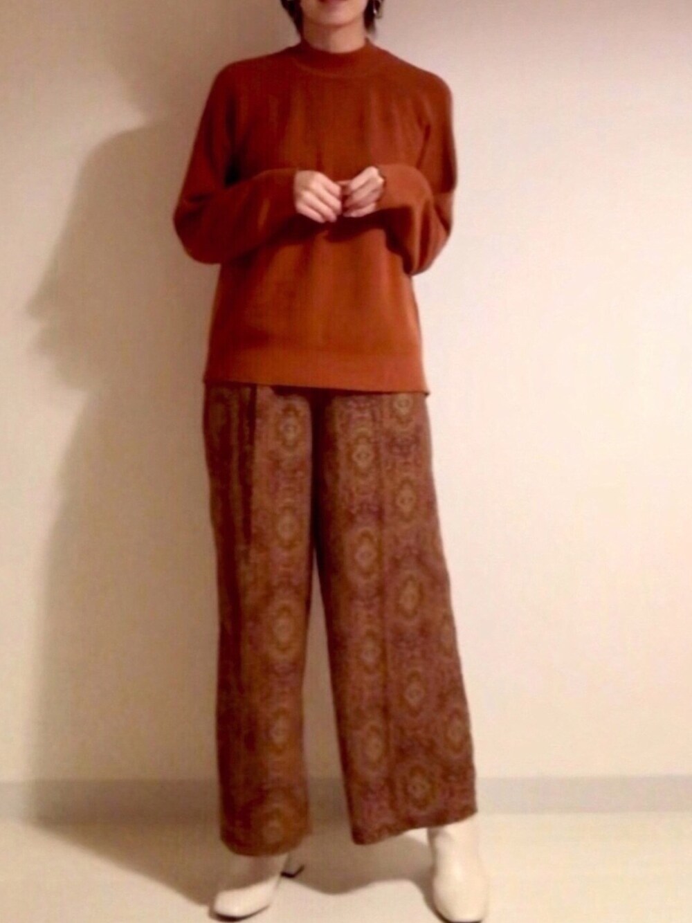 オレンジ系のニット/セーター、レッド系のその他パンツ、ホワイト系のブーツを着用したレディースの秋コーディネートの1枚目の写真