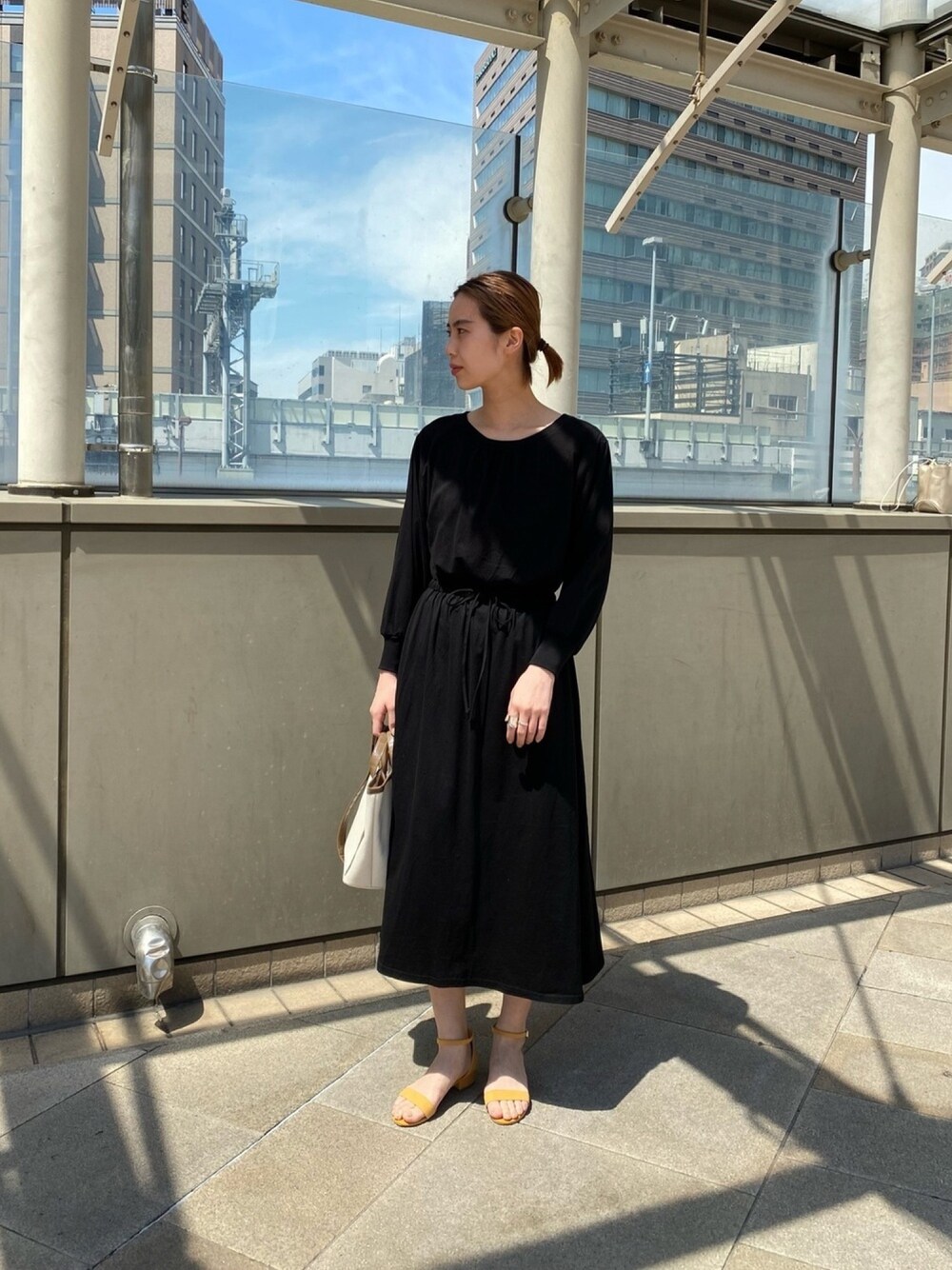ブラック系のワンピース、ブラウン系のトートバッグ、イエロー系のサンダルを着用したレディースの春コーディネートの1枚目の写真