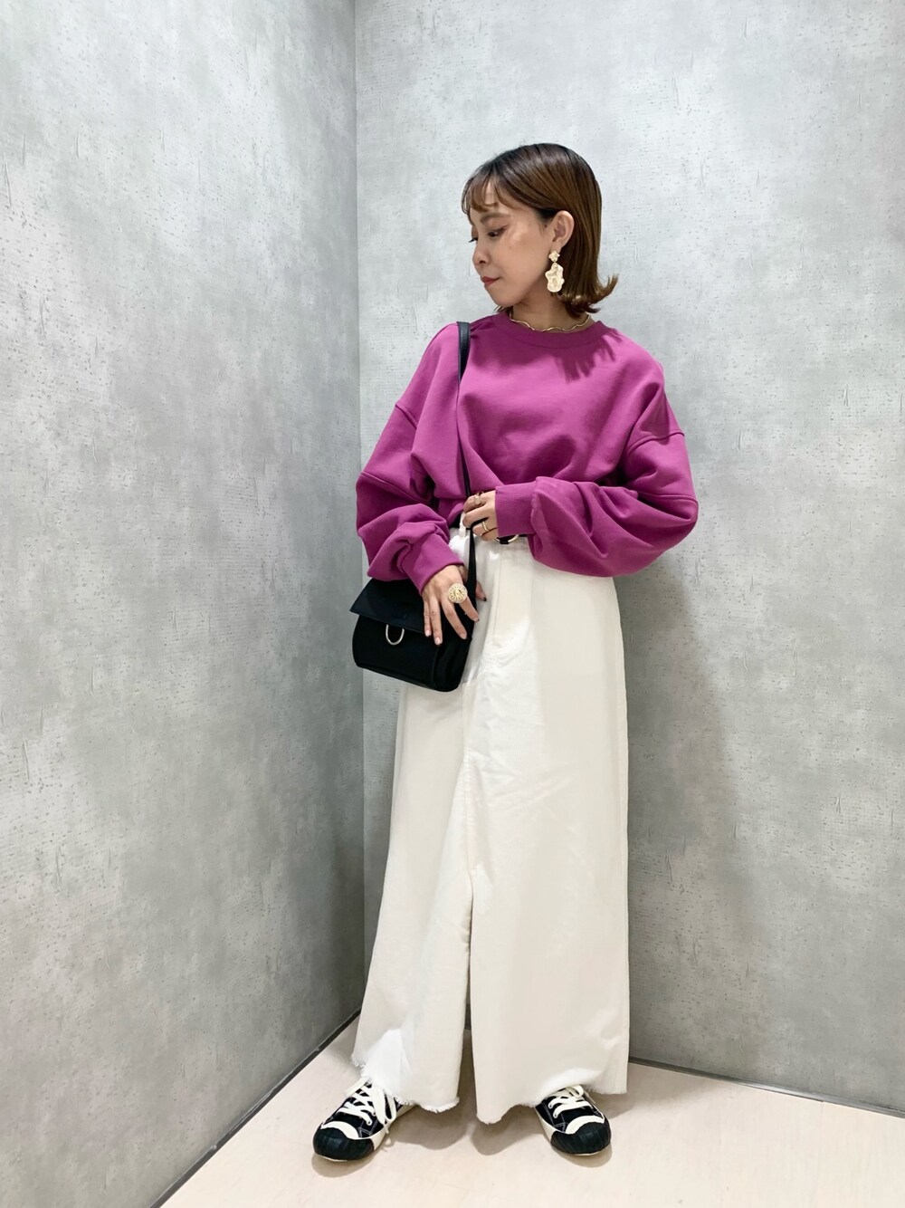 パープル系のスウェット、ホワイト系のスカート、ブラック系のスニーカーを着用したレディースの秋コーディネートの1枚目の写真