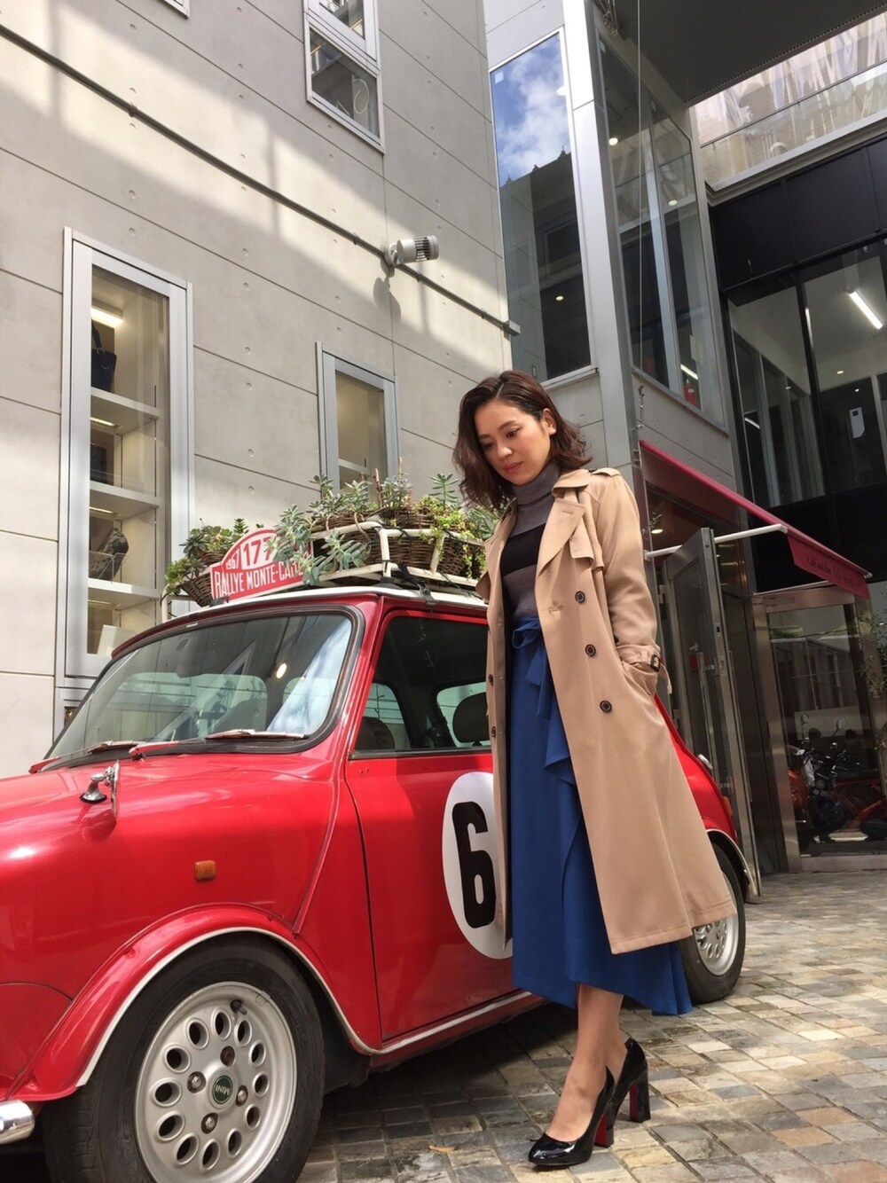 ブルー系のスカート、ベージュ系のトレンチコート、グレー系のニット/セーターを着用したレディースの秋コーディネートの1枚目の写真