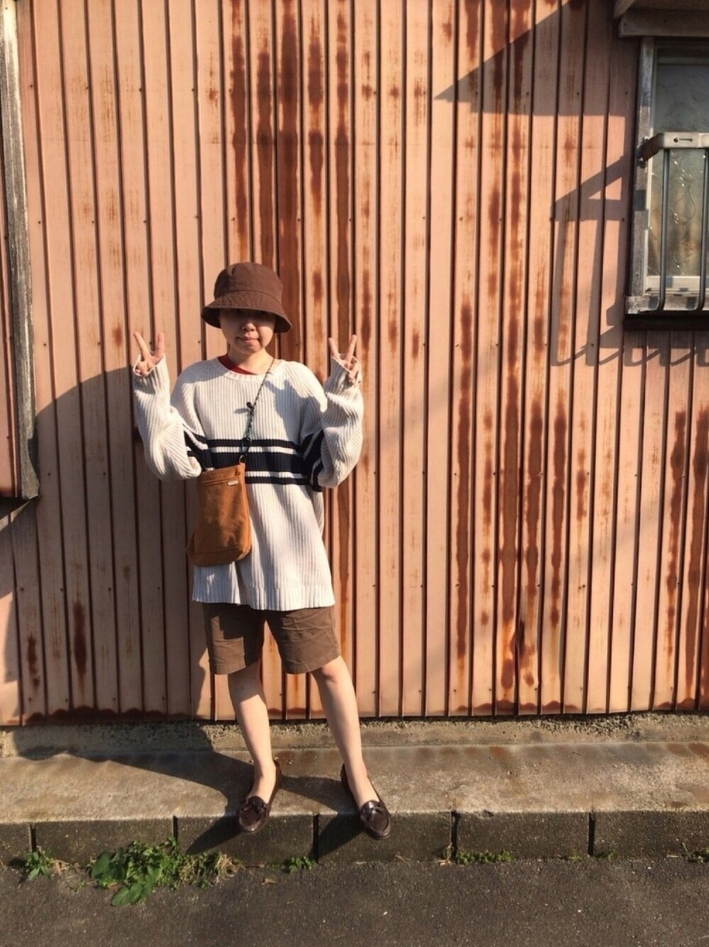 ベージュ系のニット/セーター、レッド系のTシャツ/カットソー、ブラウン系のチノパンツを着用したレディースの春コーディネートの1枚目の写真