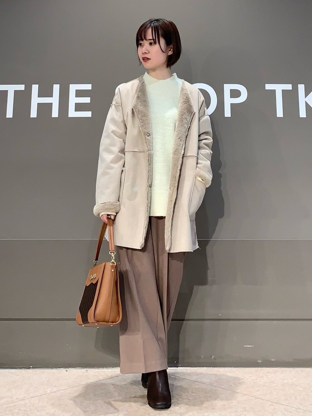 ベージュ系のノーカラーコート、ブラウン系のその他パンツ、ブラウン系のブーツを着用したレディースの冬コーディネートの1枚目の写真