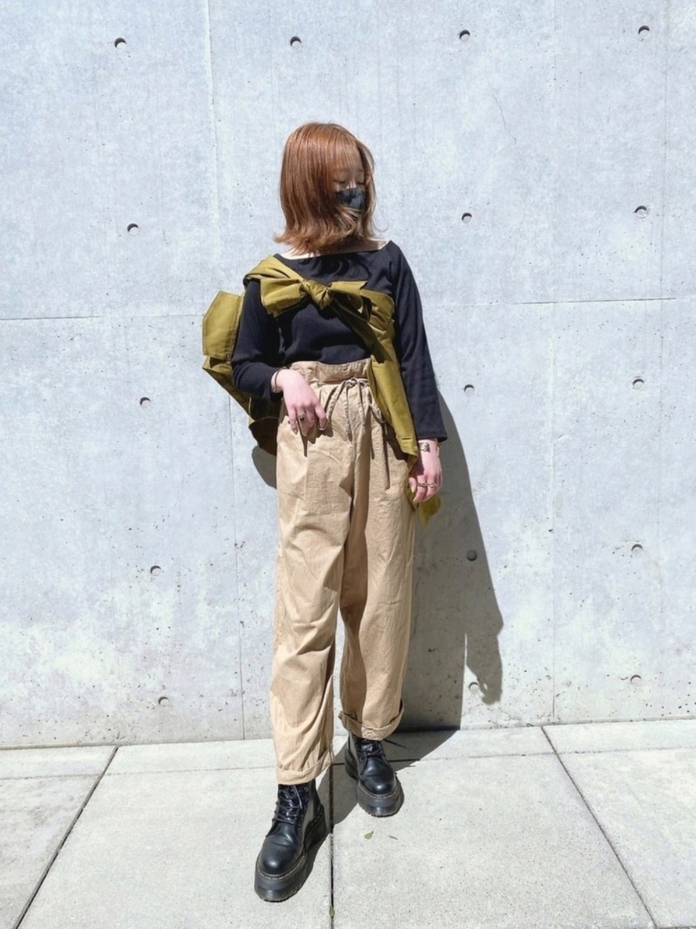 ブラック系のブーツ、ベージュ系のパンツ、グリーン系のトップスを着用したレディースの春コーディネートの1枚目の写真